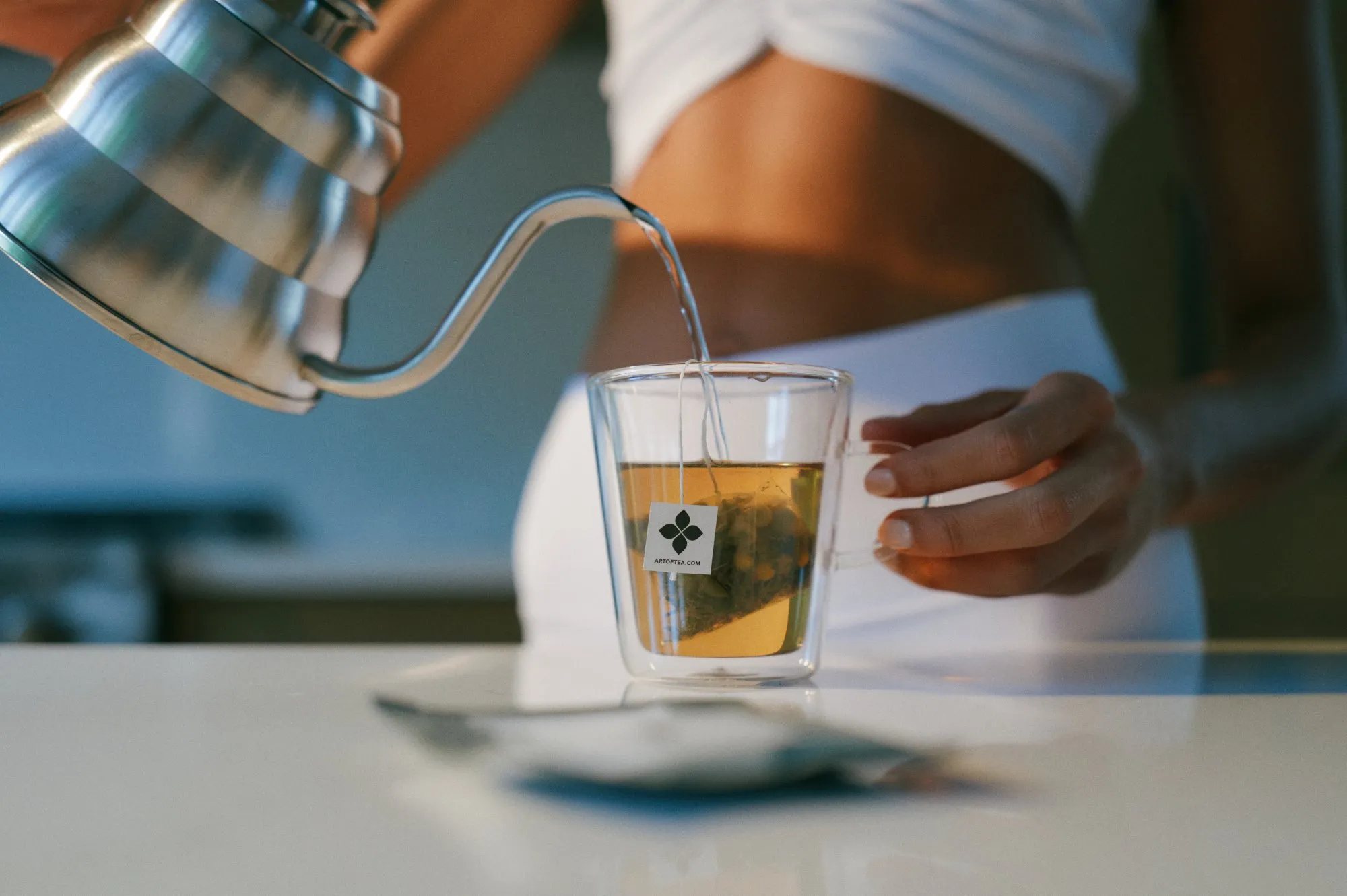 Pouring hot water from a kettle over an Art of Tea sachet in a glass mug