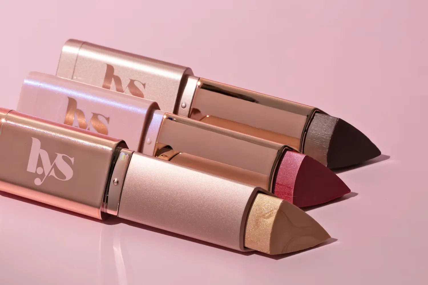 LYS Beauty lip crayons arranged on a pink backdrop